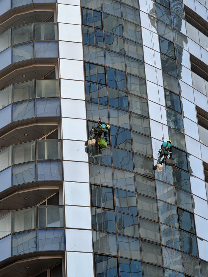 Professional window cleaners working on a skyscraper in Abu Dhabi, showcasing urban architecture.